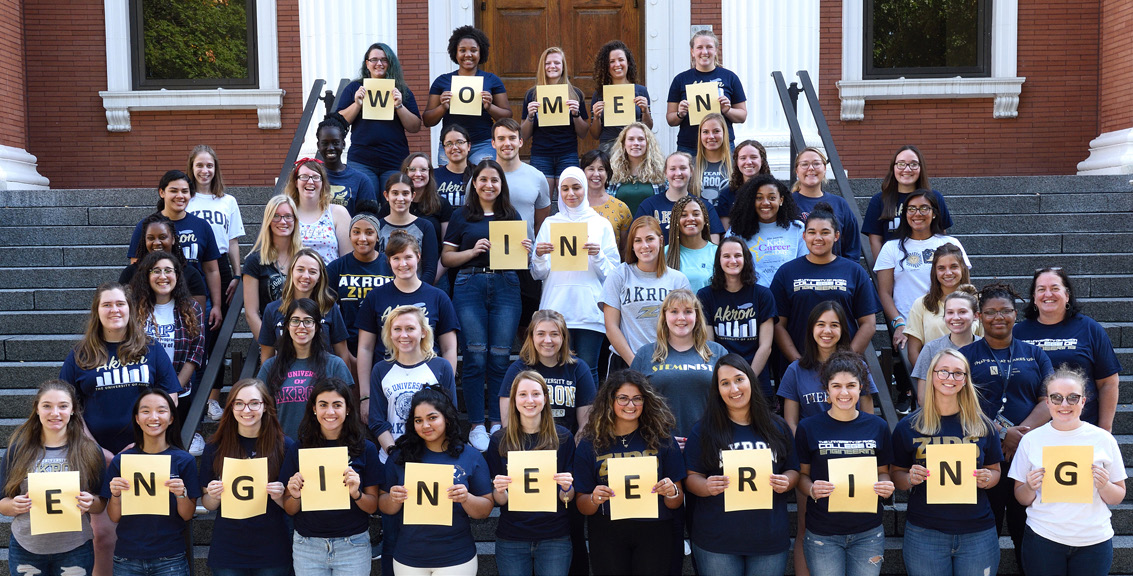 female engineering students pose on steps with a sign reading - Women in Engineering